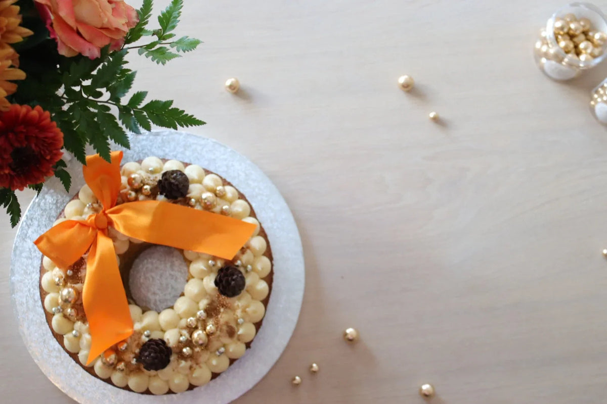 Kransformet gresskarkake med ostekrem, sjokoladekongler, gullperler og oransje satengsløyfe.