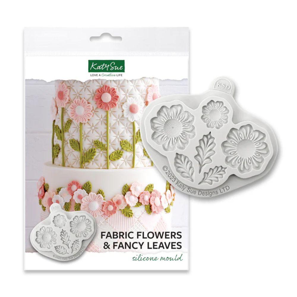 Katy Sue Fabric Flowers & Fancy Leaves silikon mold i emballasje med hvit kake dekorert med rosa sukkerbomster