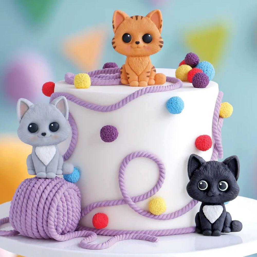 Tre fondant-katter i ulike farger på lilla kake med garnballer, laget med Katy Sue Easy Stand Cat mold