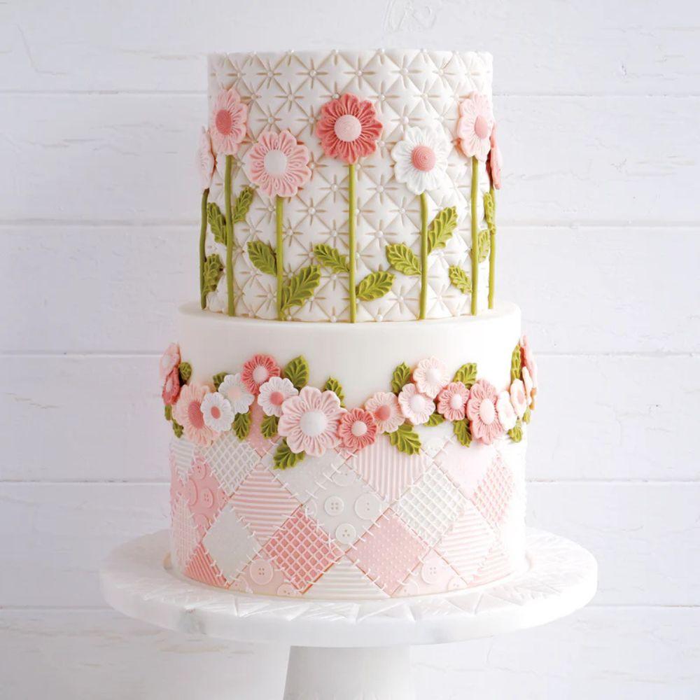 Hvit kake dekorert med rosa sukkerblomster og grønne blader laget med Katy Sue blomsterform