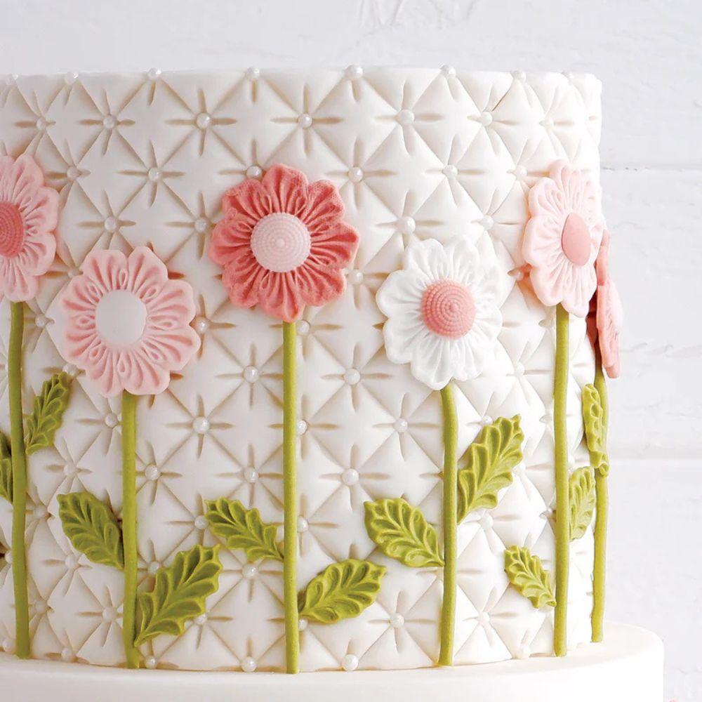 Hvit kake dekorert med rosa sukkerbomster og grønne blader laget med Katy Sue Fabric Flowers mold