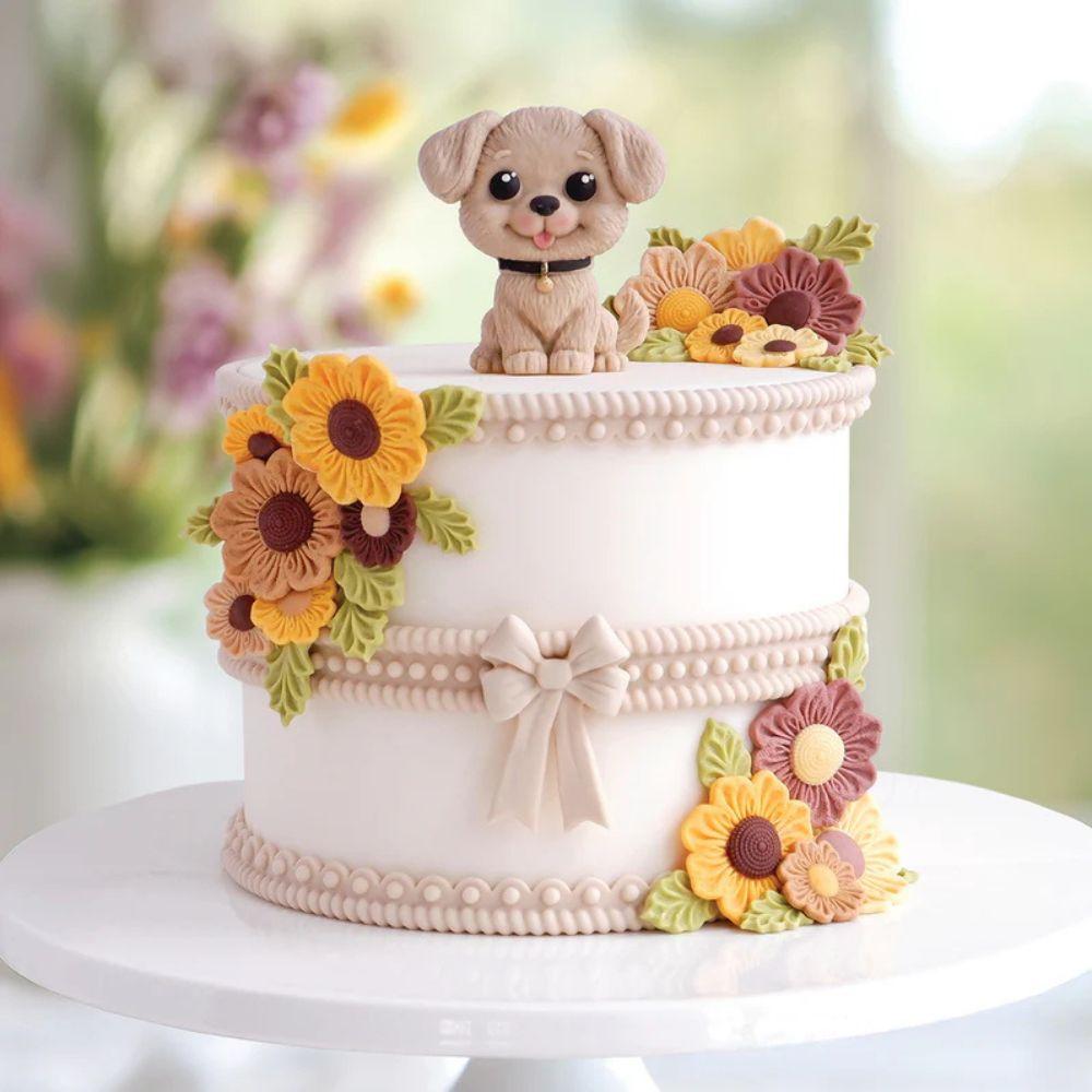 Liten fondant-hund på hvit kake dekorert med solsikker og blomster