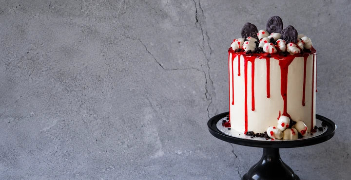 Halloweenkake med rød glasur, hodeskaller og gravsteiner på svart kakefat.