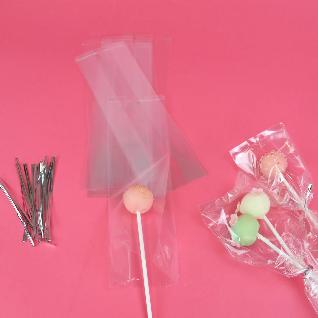 Gjennomsiktige cake pop-poser med sølvbånd og cake pops på rosa bakgrunn