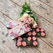 Rosa roser med grønne blader i forpakning, fotografert på trebord med en rosebukett